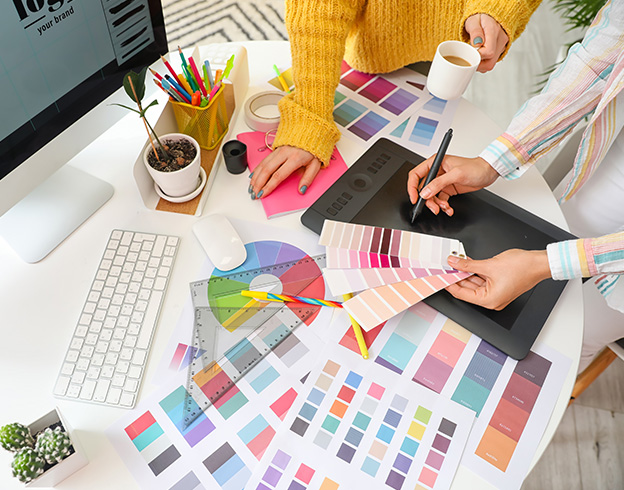 Designers collaborating on a colorful palette selection with digital tools and printed swatches.