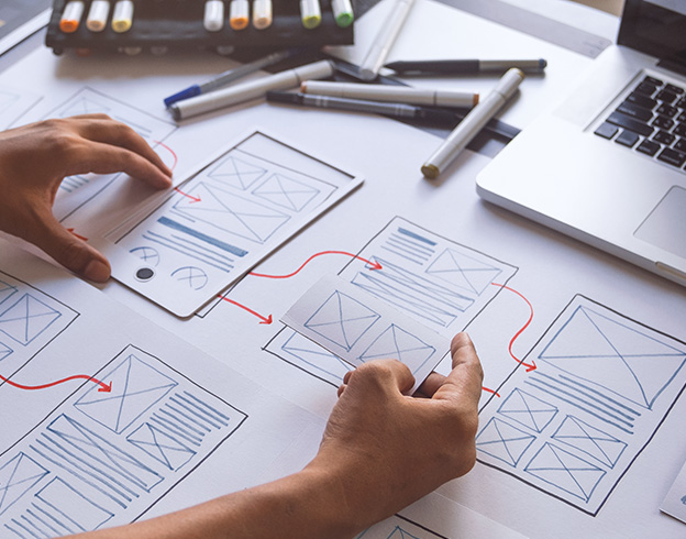 Person working on wireframes, sketching website layout with markers and open laptop.