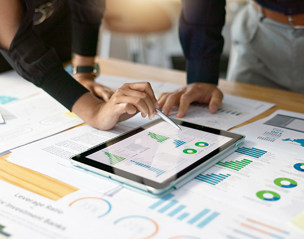 Two people reviewing financial charts and graphs on a tablet and printed documents.