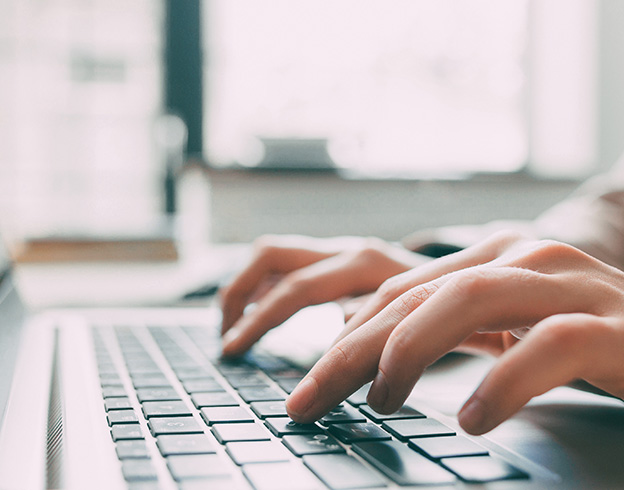 Close-up of hands typing on a laptop keyboard near a sunlit window.