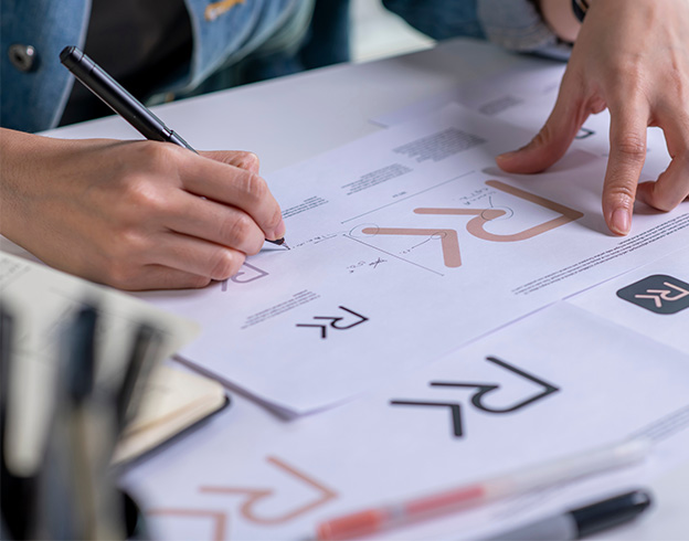 Person designs detailed logo sketches with precision using pen on paper.
